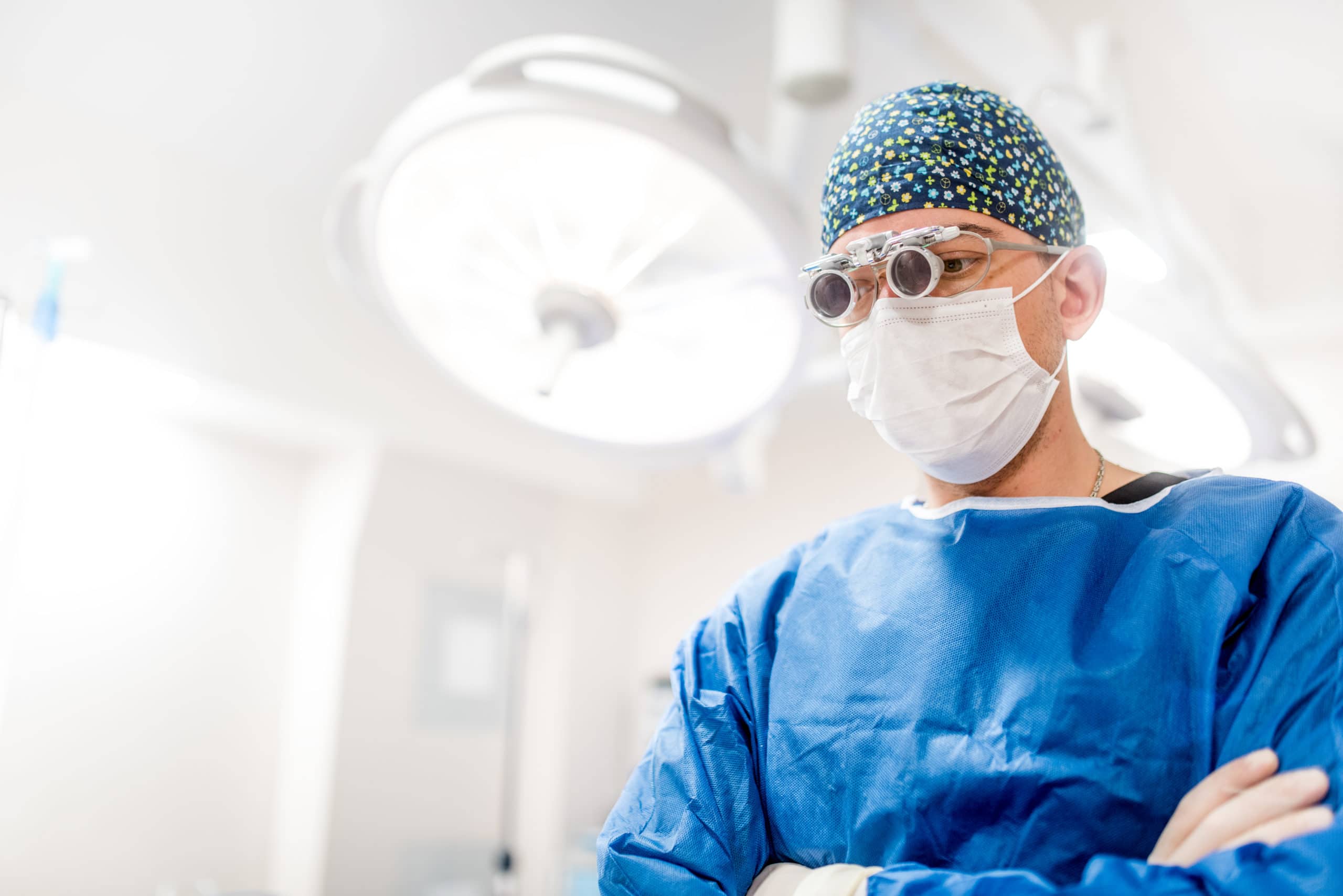 Cosmetic plastic surgeon with loupes, scrubs and rubber gloves thinking about patients